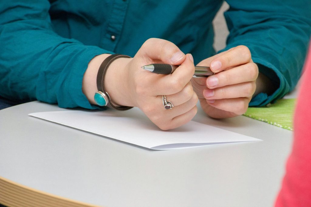 eine Person, die an einem Tisch sitzt und auf ein Stück Papier schreibt