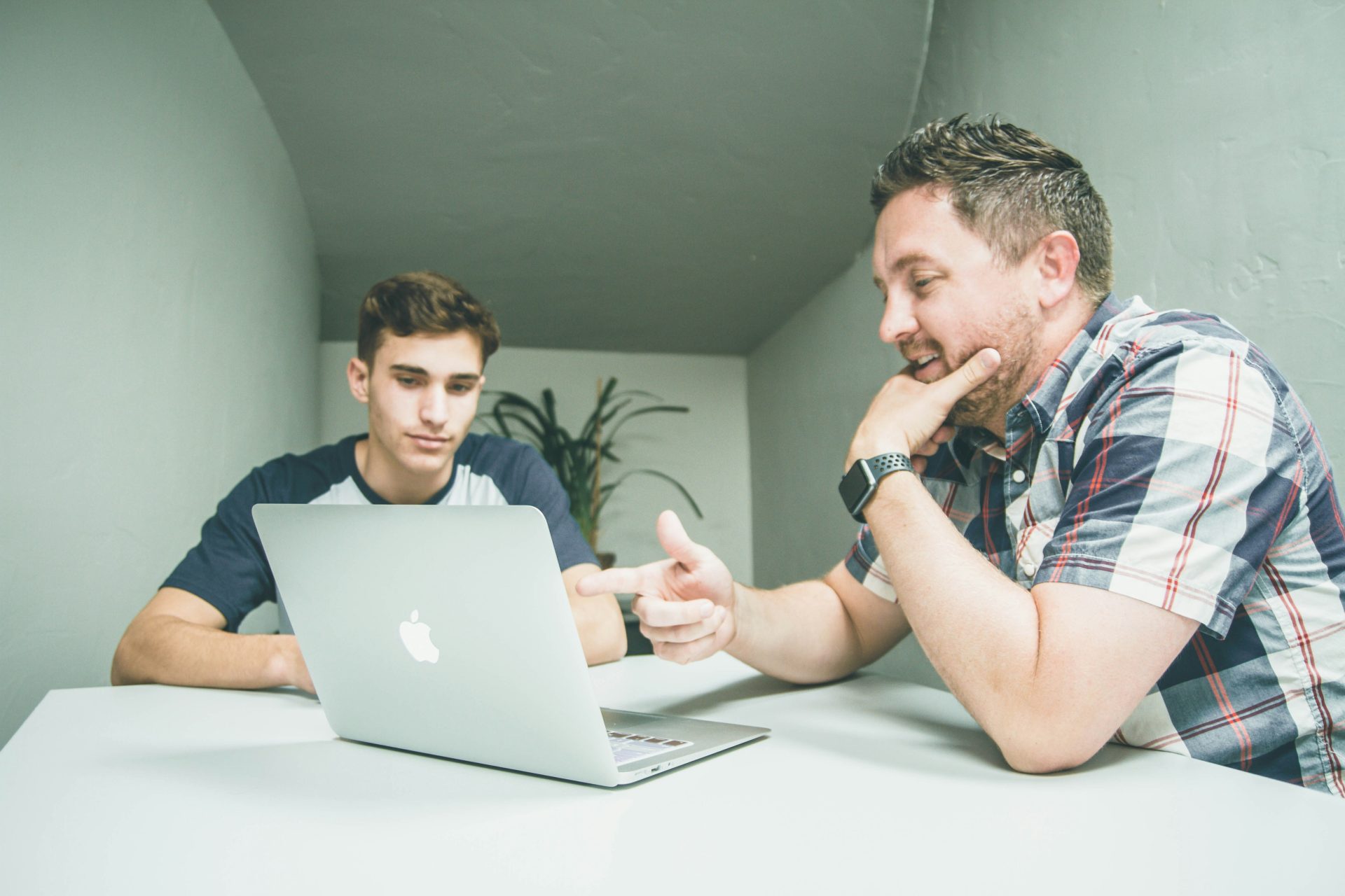 Mann in weiß-schwarz kariertem Sporthemd mit Knopfleiste zeigt auf das silberne MacBook